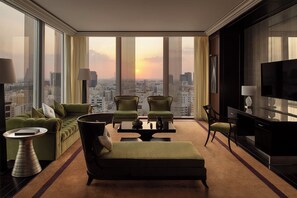 Ein Hotelzimmer in einem Hochhaus mit Blick auf die Stadt, ausgestattet mit einem Sofa, zwei Sesseln, einem Couchtisch, einem Fernseher und einem Beistelltisch.