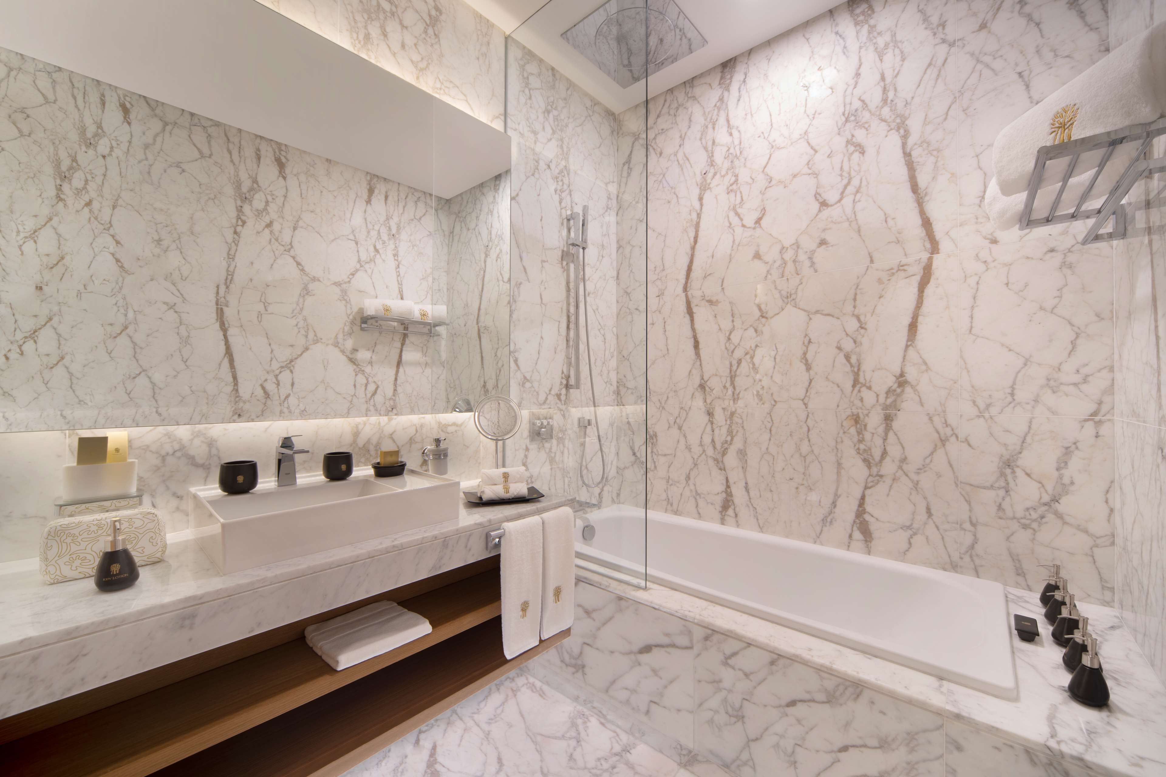 A modern bathroom with a marble backsplash, a large mirror, a double sink vanity, a bathtub, and a shower area.