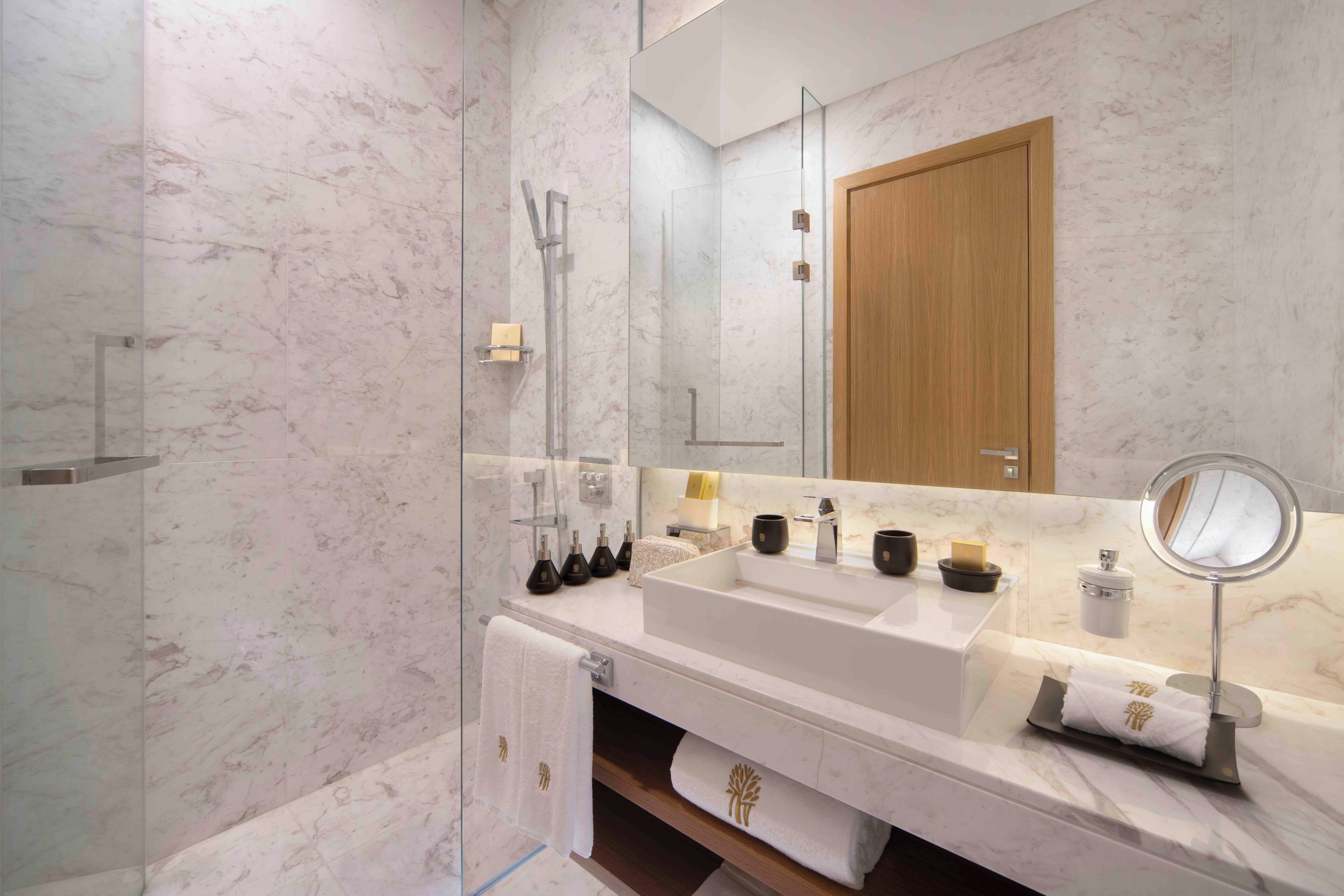 A modern bathroom with a large sink, a glass shower enclosure, and a wooden door.