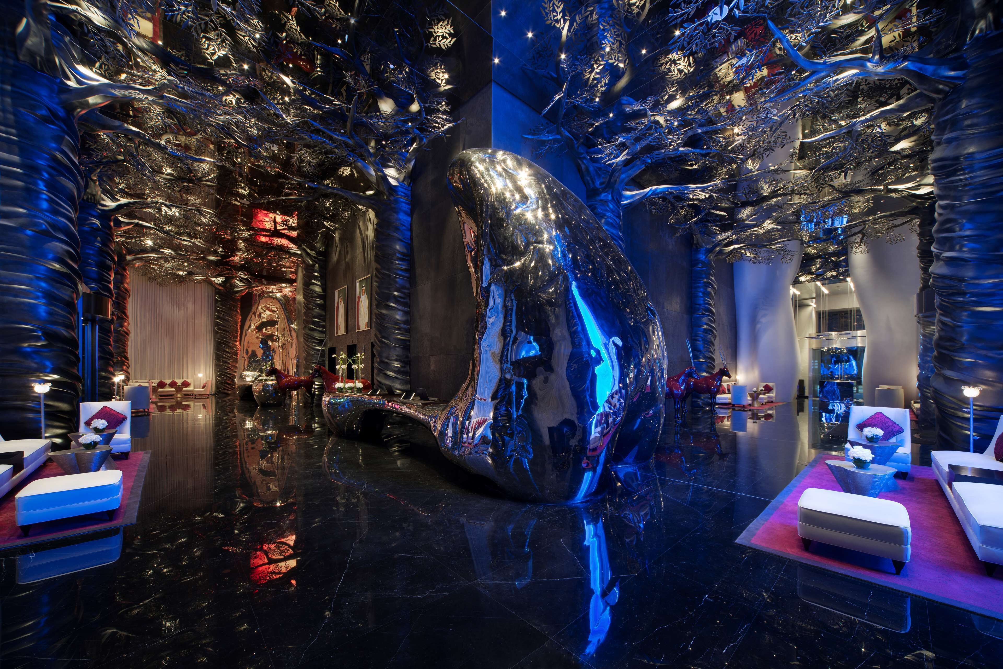 A luxurious hotel lobby with a large reflective sculpture, plush seating, and modern decor.