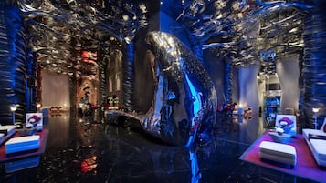 Un lobby de hotel lujoso con una gran escultura reflectante, asientos cómodos y decoración moderna.