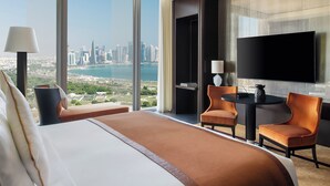 A hotel room with a large bed, two chairs, a small table, a TV, and a view of a cityscape and water. - Banyan Tree Doha at La Cigale Mushaireb (Doha)
