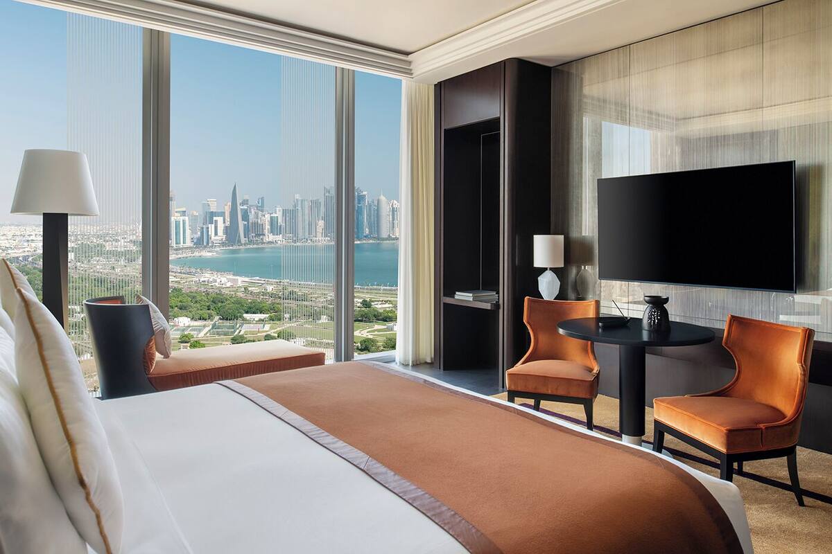 Habitación de hotel con una cama grande, dos sillas, una mesita, televisión y vistas a la ciudad y al agua.