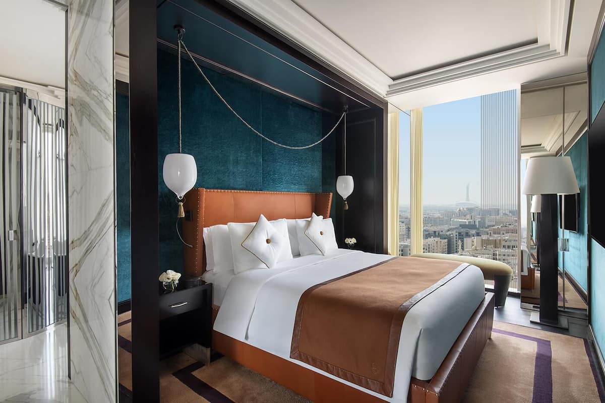 Ein modernes Hotelzimmer mit großem Bett, Blick auf die Stadt, Marmorböden und einer dunkelblauen Akzentwand.