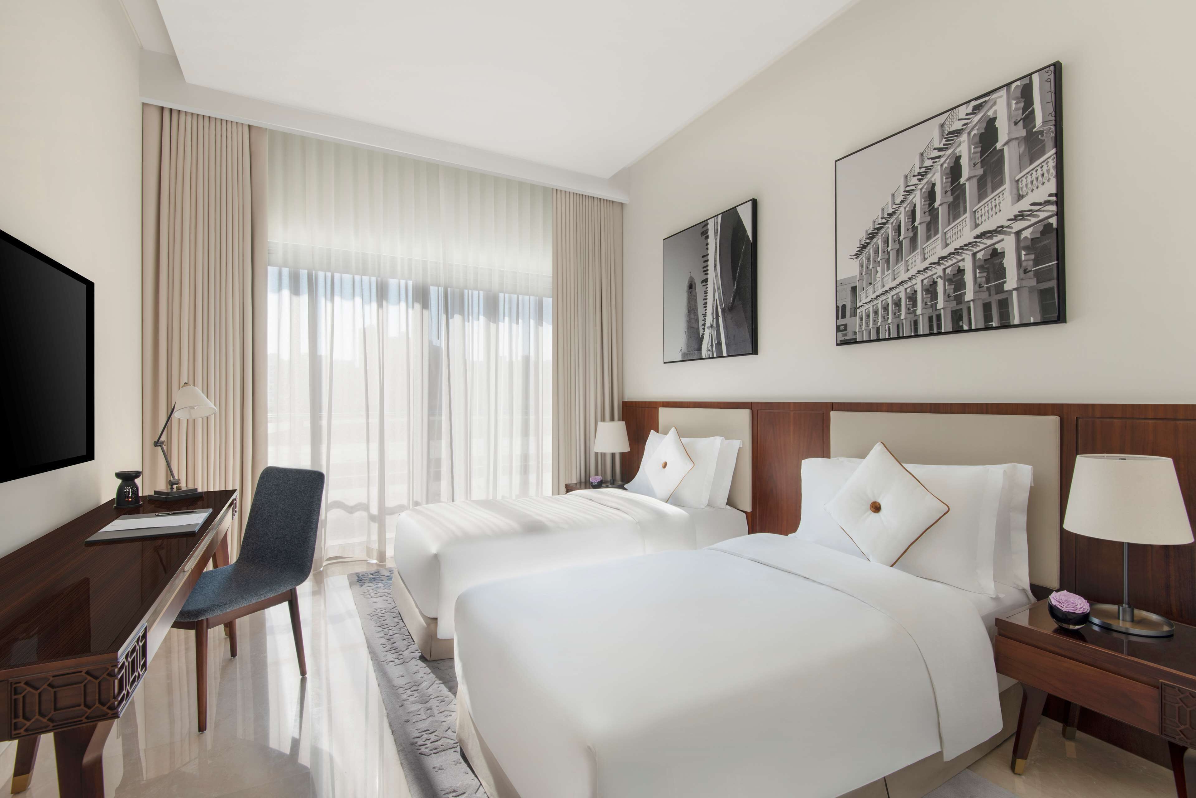 Habitación de hotel con dos camas, un escritorio, una silla, un televisor y dos cuadros en la pared.