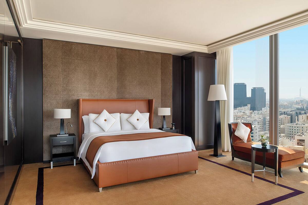 Habitación de hotel moderna con una cama grande, dos mesitas de noche, una silla y vistas a la ciudad.