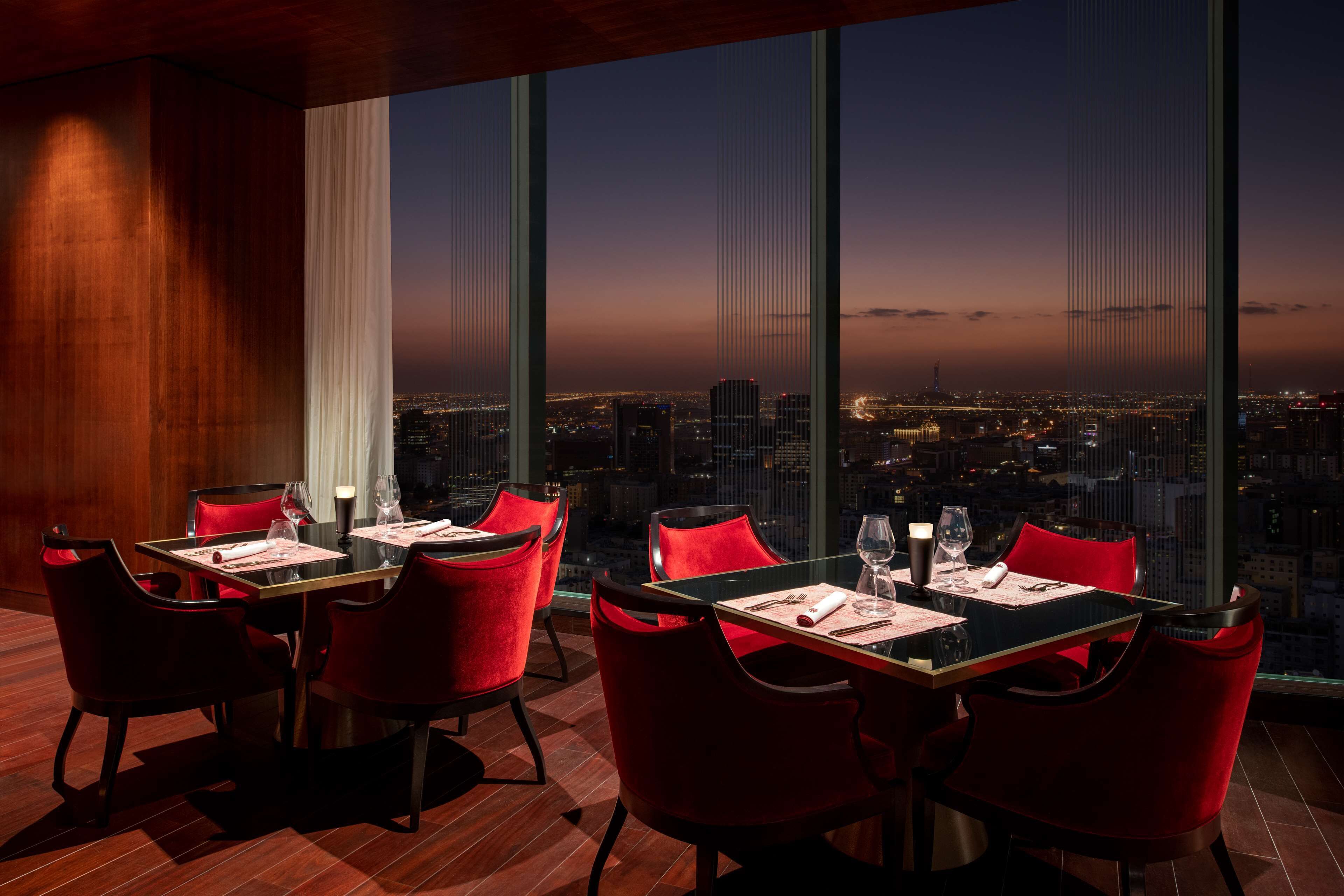 A dining area with tables and chairs, large windows offering a city view, and a modern interior design.