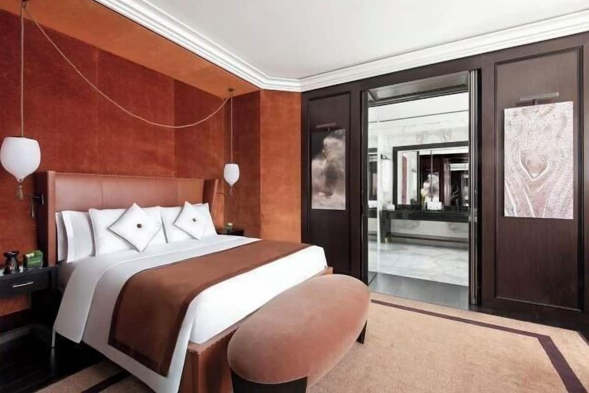 Ein Hotelzimmer mit einem großen Bett, einer Bank, einem Nachttisch und einer Tür zu einem Flur.