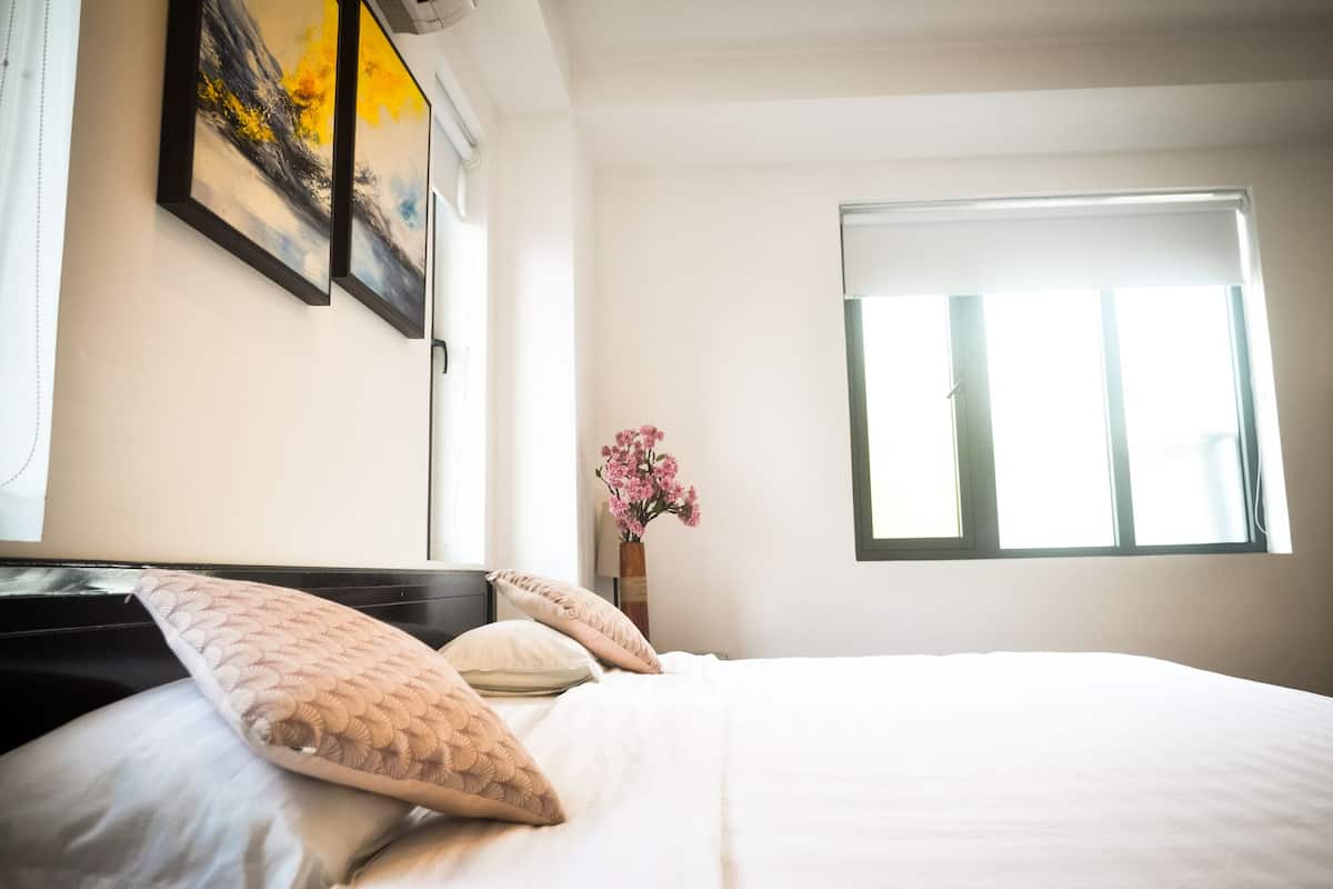Un dormitorio con cama, almohadas, un florero con flores y obras de arte en la pared.