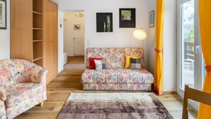 En hyggelig stue med en blomstret sofa, et træskab og udsigt til det fri gennem et stort vindue.