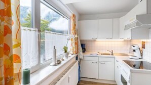 Et moderne køkken med hvide skabe, indbygget ovn og et vindue med orange gardiner.