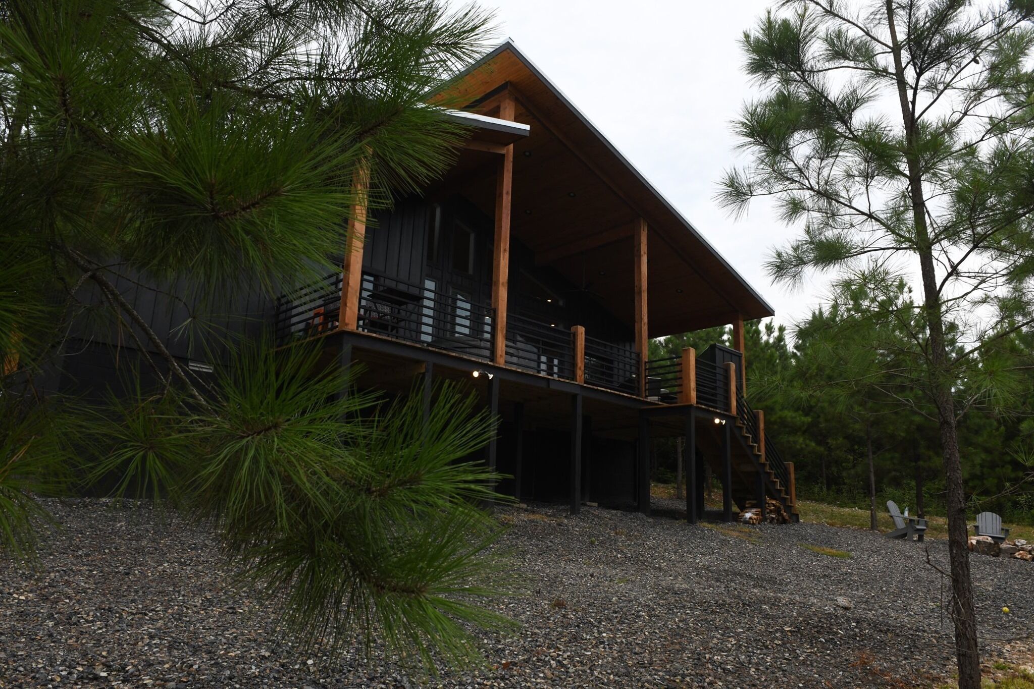A cabin with a wooden exterior, a covered deck, and a gravel ground.