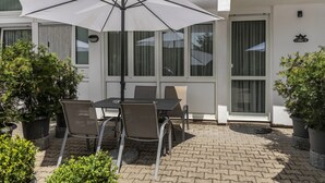 Une terrasse extérieure avec une table et des chaises, un parasol blanc et des plantes en pot.