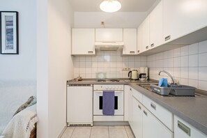 Une cuisine de taille réduite avec des meubles blancs, une cuisinière, un évier et une bouilloire.