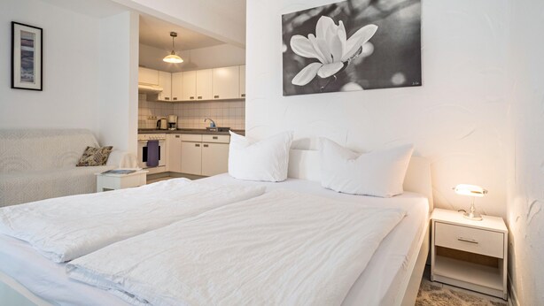 Une chambre à coucher avec un lit, une table de chevet et un tableau représentant une fleur, accroché au mur.