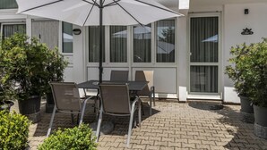 Une terrasse extérieure avec une table et des chaises, un parasol blanc et des plantes en pot.