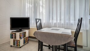 Une pièce comprenant un téléviseur posé sur un meuble, une table à manger avec des chaises et une bibliothèque.