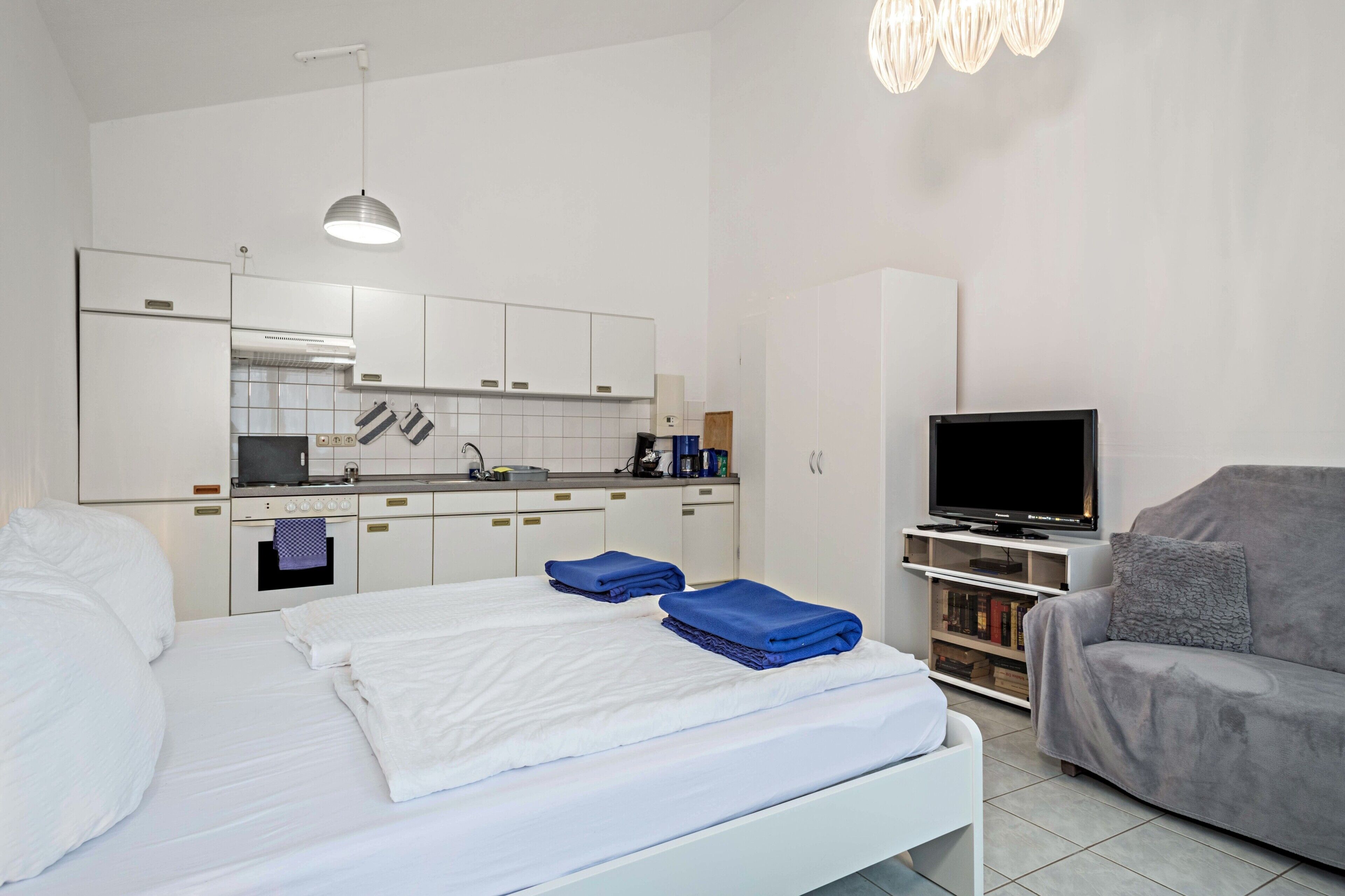 Ein Hotelzimmer mit Bett, Fernseher, Sofa, Küchenzeile und Deckenleuchte.