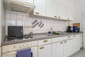 A kitchen with white cabinets, a stove, a sink, and hanging utensils.