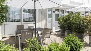 Eine Terrassengruppe draußen mit Tisch und Stühlen, umgeben von Topfpflanzen und Sonnenschirmen.