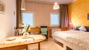Ein Zimmer mit einem Bett, einem Tisch mit einer Vase, einem Stuhl und einem Fenster mit Vorhängen.