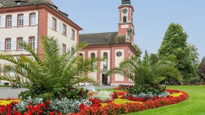 Ein Gebäude mit einem Glockenturm, einem Garten mit roten und weißen Blumen sowie Palmen.