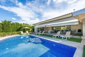 Una piscina con borde de baldosas, sillas de descanso y un patio con mobiliario exterior.