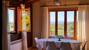Un comedor con una mesa y sillas, vistas al paisaje y un ventanal con cortinas.