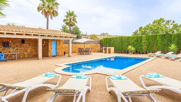 Zona de piscina con sillones de descanso y un edificio de piedra con puerta azul.