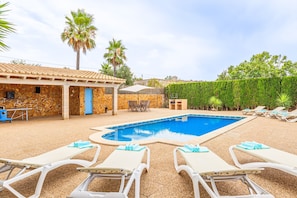 A swimming pool area with lounge chairs and a stone building with a blue door.
