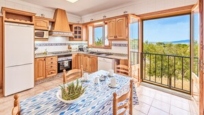 Una cocina moderna con armarios de madera, una mesa de comedor preparada para cuatro comensales y vistas al paisaje a través de grandes ventanales.