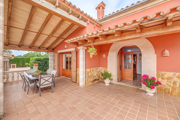 A covered patio with a table and chairs, a stone wall, and a wooden door.
