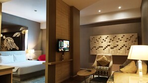 A modern hotel room with a bed, a TV, a seating area with a chair and a sofa, and a decorative wall panel. - The MELIO Enim (Muara Enim)