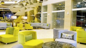 A modern lobby with yellow and grey sofas, a central coffee table, and geometric ceiling lighting. - The MELIO Enim (Muara Enim)