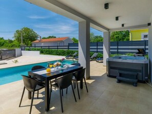 Una cocina exterior moderna con piscina, zona de comedor y sillones de descanso.