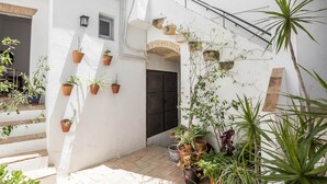 A white-walled courtyard with potted plants, a staircase, and a door.