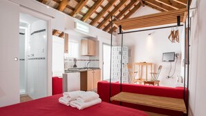 Una habitación de hotel moderna con una cama, un sofá rojo, techo de madera y una kitchenette al fondo.