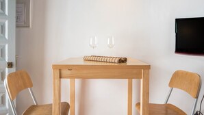 Una pequeña mesa de madera con dos sillas, un esterilla enrollada y dos copas de vino sobre la mesa.