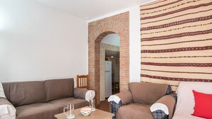 Een woonkamer met een bakstenen boog, een bank, een tafel met glazen en een schaal, en een kamer met een patroon op de muur.