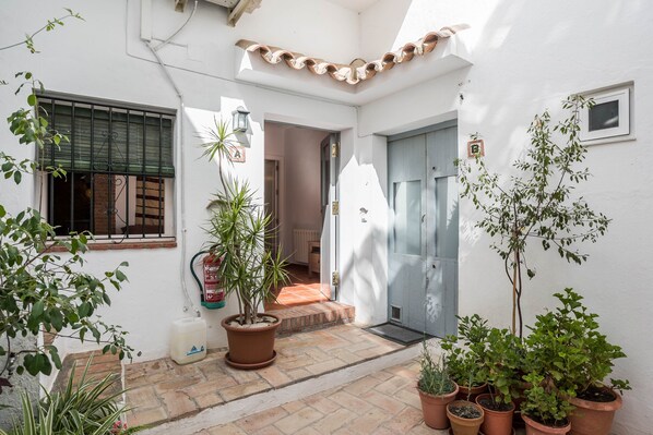Un patio con plantas en macetas, suelo de baldosas y una puerta que da a un espacio interior.