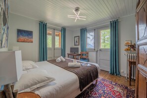 Et hotelværelse med seng, skrivebord, stol, tv og et vindue med gardiner.