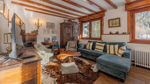 Ein gemütliches Wohnzimmer mit Holzbalken, einem blauen Sofa, einem Kuhfellteppich und einem Holztisch.