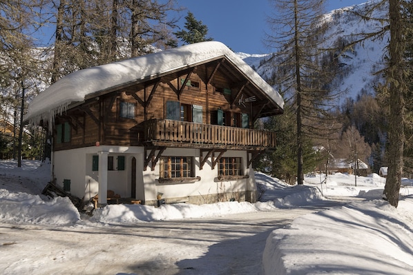 Un chalet en bois doté d’un balcon, entouré de neige et d’arbres.