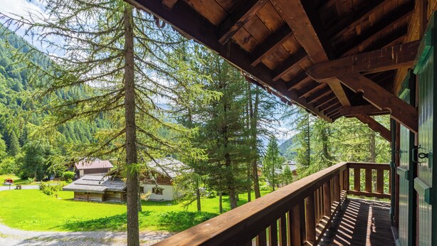 Ein Holzbalkon mit Blick auf ein bewaldetes Gebiet und ein Gebäude im Hintergrund.