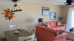 A living room with a dining table, white chairs, a pink sofa with floral cushions, and two framed pictures on the wall. - Villa A2, Beach front, ground level! (Eastpoint)