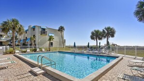 A rectangular pool with a metal ladder, surrounded by lounge chairs and umbrellas, with a building in the background. - Villa A2, Beach front, ground level! (Eastpoint)