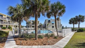 A pool area with a wooden deck, palm trees, and a building with balconies. - Villa A2, Beach front, ground level! (Eastpoint)