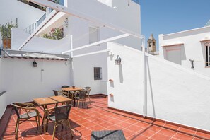 Una terraza con una mesa y sillas, un muro blanco y una torre campanario al fondo.