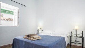 A hotel room with a bed, two bedside lamps, a window with a curtain, and a wall-mounted shelf. - Holiday Apartment "Casa La Costanilla D" with Roof Terrace and Air Conditioning (Vejer de la Frontera)