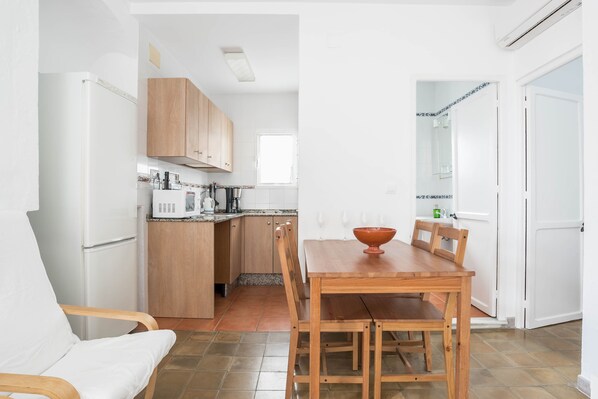 Una cocina compacta con armarios de madera, un refrigerador blanco, una mesa de comedor con sillas y una ventana.